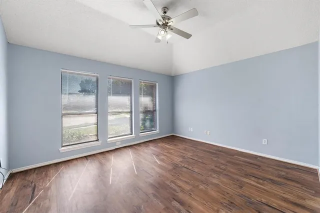 an empty room with wooden floor chandelier fan and windows
