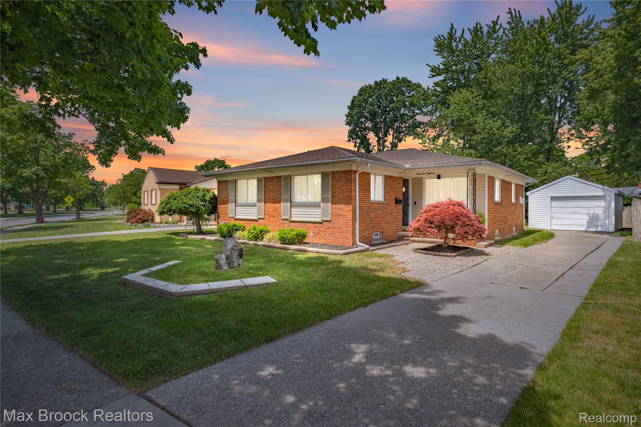 Brick ranch-style residence featuring a detached garage, established front landscaping, and a paved driveway