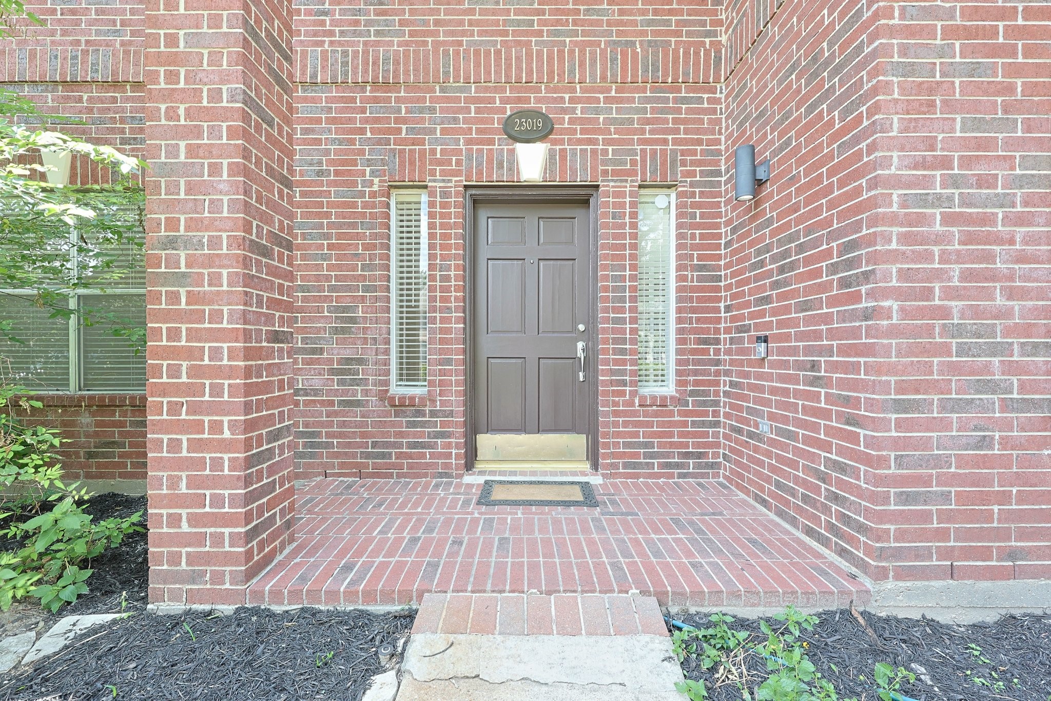 23019 Eastgate Village Drive Spring, TX 77373 - Photo 38 of 46 Welcoming brick exterior with a central dark brown door flanked by tall narrow windows. The entryway is framed by a covered porch, offering a classic and inviting appearance.
