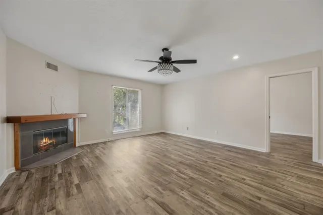 a view of an empty room with wooden floor fireplace and a window