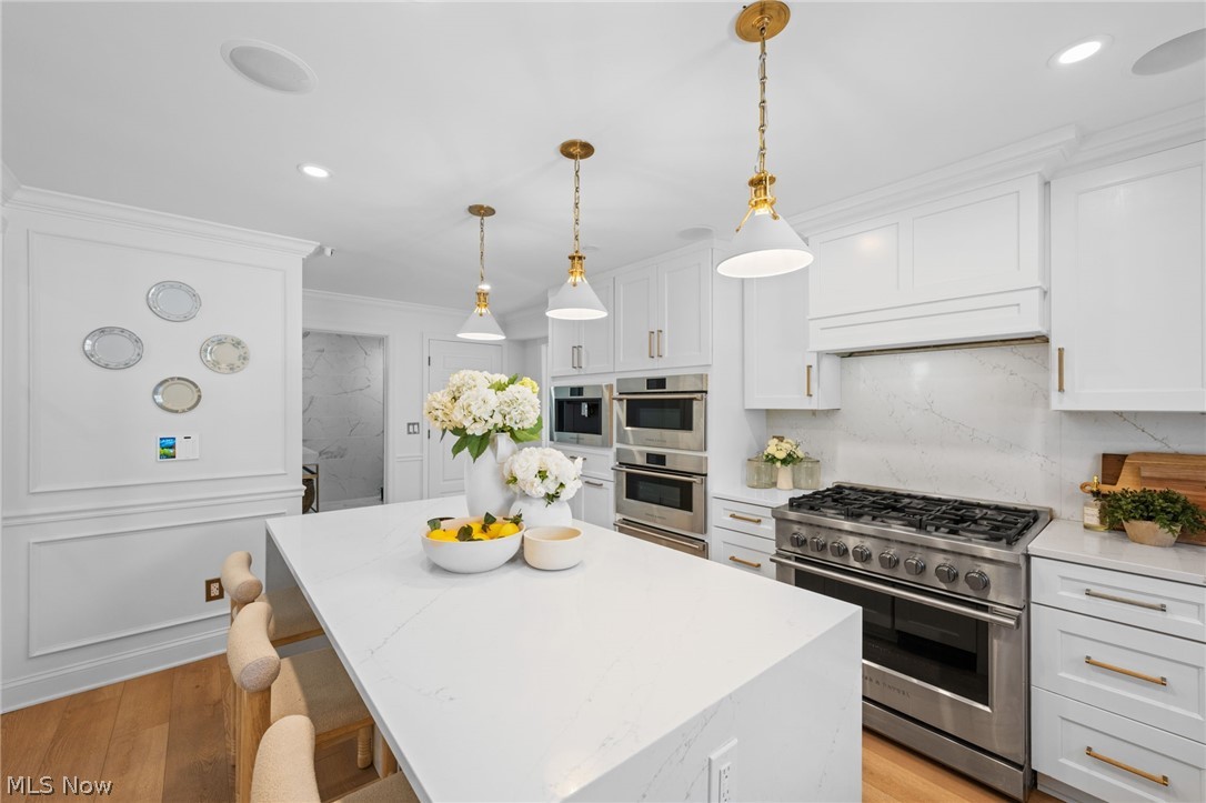 25870 Kennedy Ridge Road North Olmsted, OH 44070 - Photo 16 of 50 Modern kitchen featuring a large center island with a stone-finish countertop, stainless steel appliances, white cabinetry with brass hardware, and recessed lighting