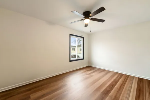 an empty room with wooden floor ceiling fan and windows