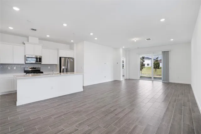 a large kitchen with stainless steel appliances granite countertop a refrigerator a stove a sink and white cabinets with wooden floor