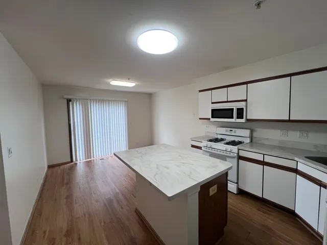 a kitchen with stainless steel appliances granite countertop a stove top oven a sink dishwasher and a refrigerator with wooden floor