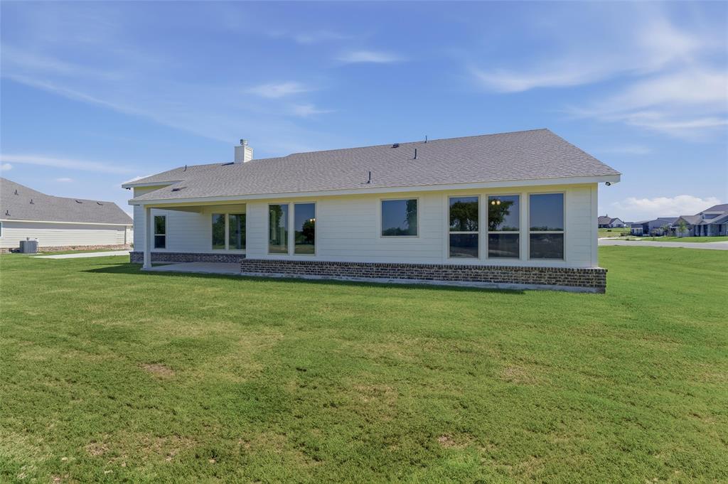 130 Fossil Canyon Drive Rhome, TX 76078 - Photo 22 of 25 Rear exterior featuring a covered patio, multiple windows, light-colored siding, and a brick base