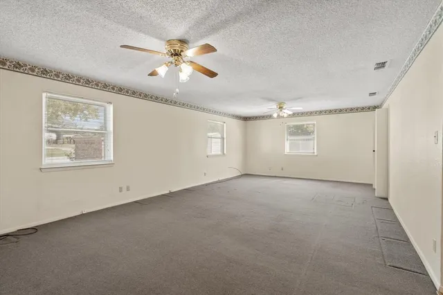 an empty room with chandelier fan and windows