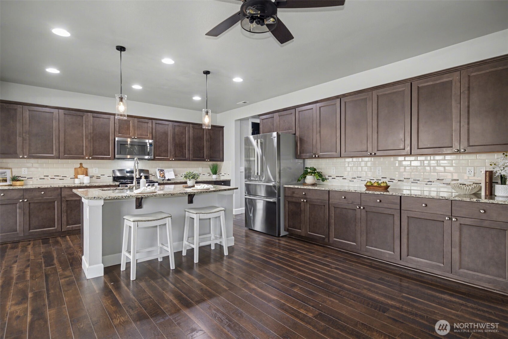 207 Fielding Street Northeast Orting, WA 98360 - Photo 8 of 37 a kitchen with kitchen island granite countertop wooden floors white cabinets and stainless steel appliances