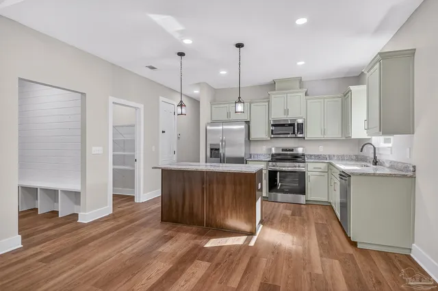 a kitchen with stainless steel appliances kitchen island granite countertop a stove a sink a refrigerator and white cabinets with wooden floor