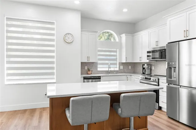 a kitchen with stainless steel appliances granite countertop a microwave a stove a sink dishwasher and white cabinets with wooden floor