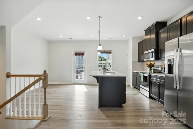 a open kitchen with stainless steel appliances granite countertop a refrigerator a stove top oven a sink dishwasher a dining table and chairs with wooden floor