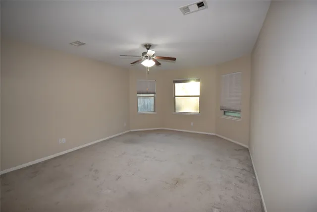 an empty room with chandelier fan and windows
