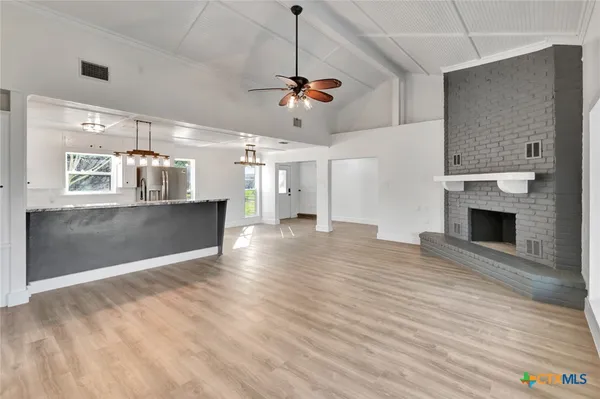 a view of a livingroom with a fireplace a ceiling fan and wooden floor