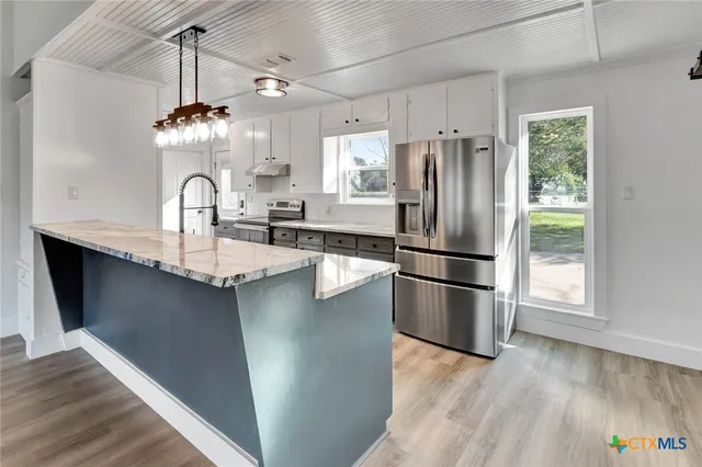 a kitchen with stainless steel appliances granite countertop a refrigerator a sink dishwasher a stove and a dining table with wooden floor