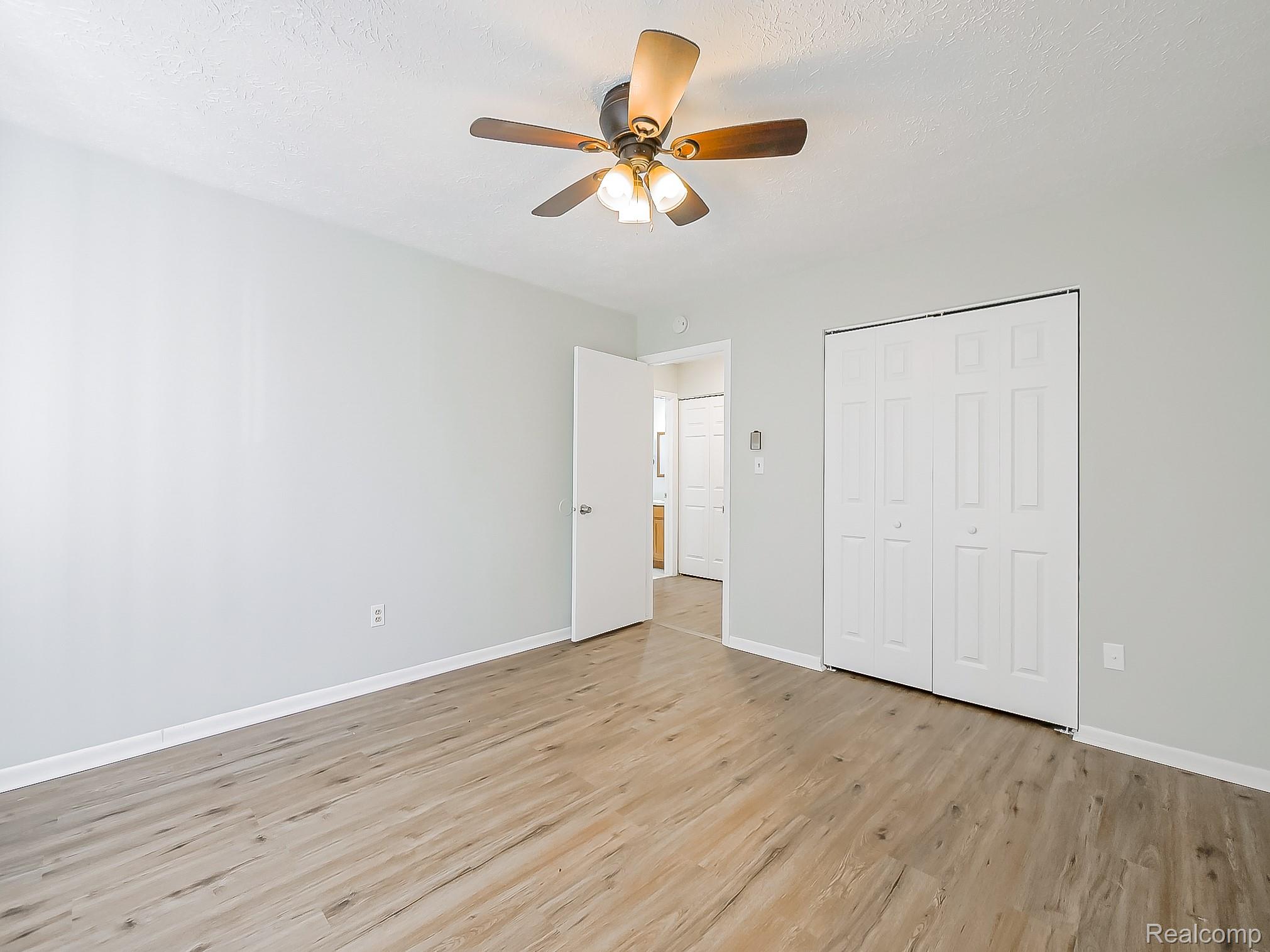 125 East Van Riper Road, Unit 7 Fowlerville, MI 48836 - Photo 15 of 26 Unfurnished bedroom with a closet, light wood-type flooring, a ceiling fan, and a textured ceiling