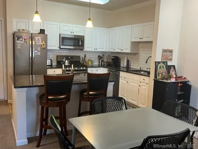 a kitchen with stainless steel appliances kitchen island granite countertop dining table chairs and a refrigerator