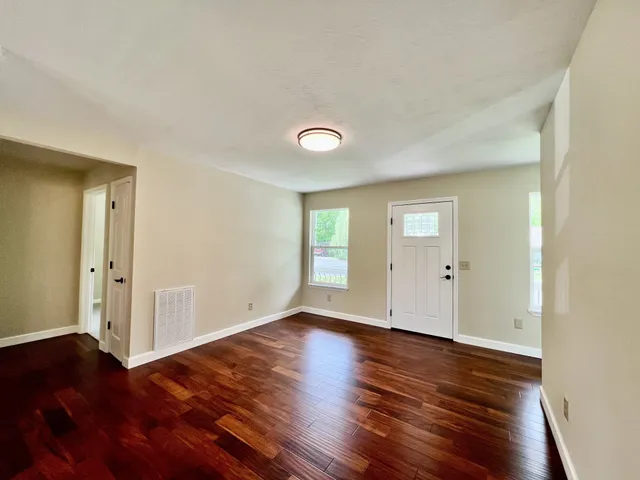 a view of an empty room with wooden floor and a window