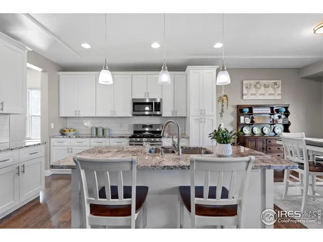 a kitchen with kitchen island granite countertop a stove a sink a refrigerator and white cabinets with wooden floor