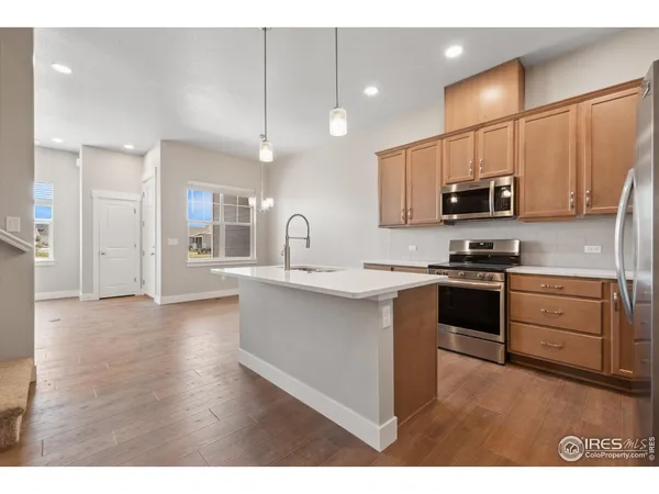 a kitchen with stainless steel appliances a stove top oven a sink a refrigerator white cabinets and a wooden floor