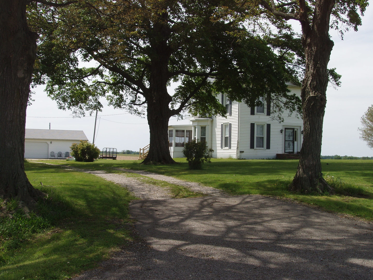 a view of a white house next to a big yard and large trees