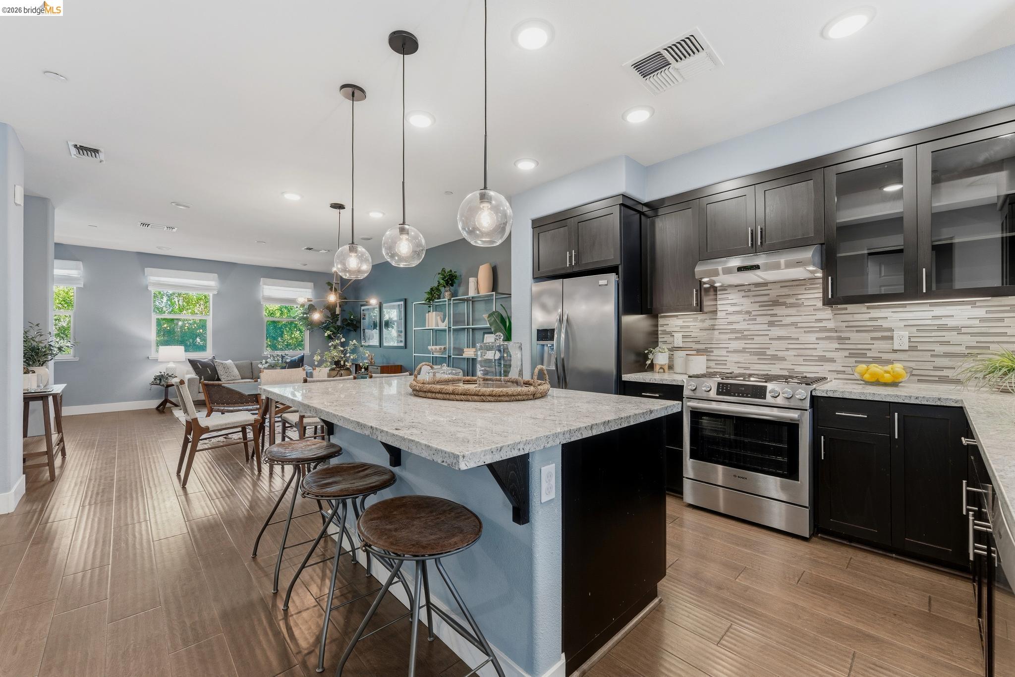 Kitchen with stainless steel appliances, a center island, a kitchen breakfast bar, glass fronted cabinets, and light wood finished floors