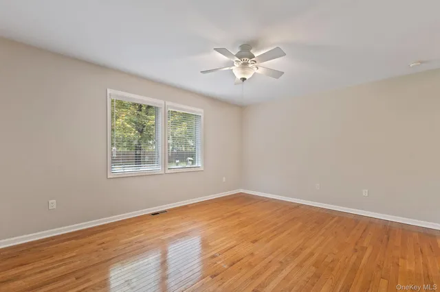 an empty room with wooden floor chandelier fan and windows