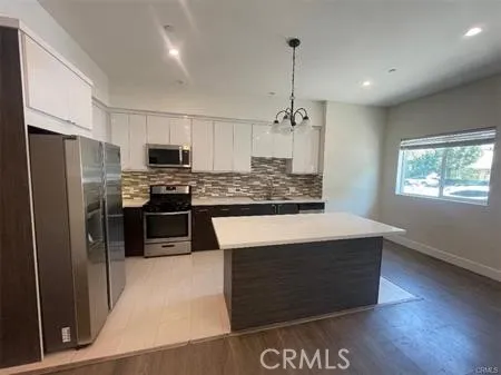 a kitchen with stainless steel appliances kitchen island granite countertop a stove a refrigerator a sink a oven with wooden floor and cabinets