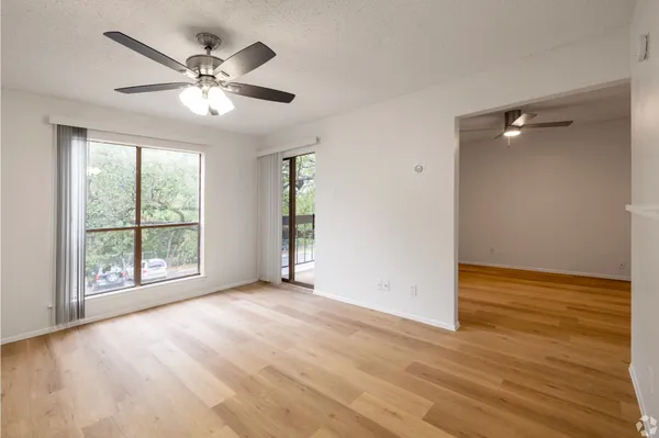 an empty room with wooden floor fan and windows