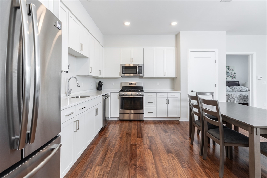 3531 Washington Street, Unit 322D Boston, MA 02130 - Photo 2 of 24 a kitchen with granite countertop a refrigerator a stove a sink dishwasher a dining table and chairs with wooden floor