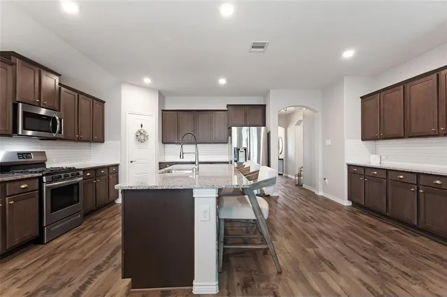 a kitchen with stainless steel appliances granite countertop a stove top oven a sink dishwasher a dining table and chairs with wooden floor