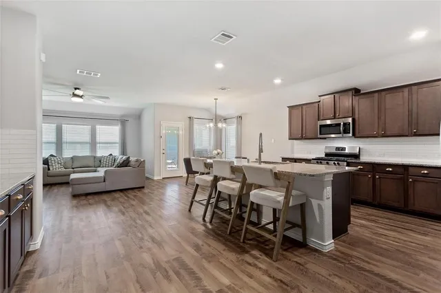 a living room with stainless steel appliances granite countertop furniture wooden floor and a kitchen view