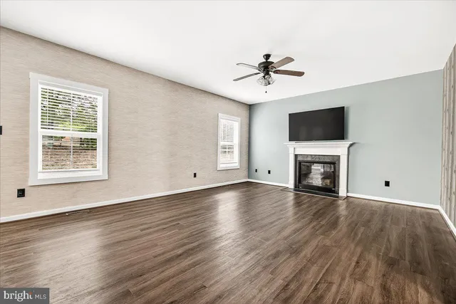 a view of a livingroom with a fireplace window a ceiling fan and wooden floor