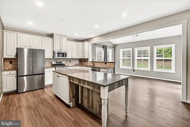 a kitchen with stainless steel appliances granite countertop a refrigerator a sink dishwasher a stove and a refrigerator with wooden floor