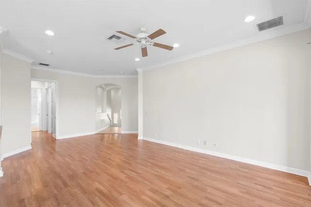 a view of an empty room with wooden floor and a ceiling fan