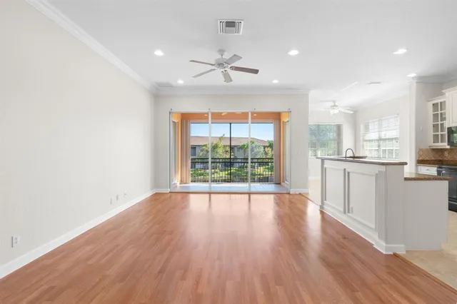 a view of an empty room with wooden floor and a kitchen