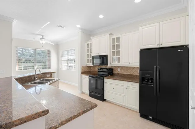 a kitchen with stainless steel appliances granite countertop a refrigerator a sink a stove and white cabinets with wooden floor