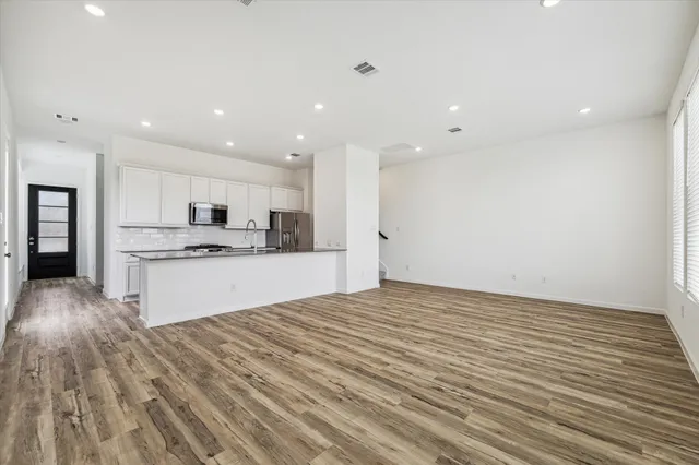 a large white kitchen with kitchen island a sink dishwasher a refrigerator and white cabinets with wooden floor