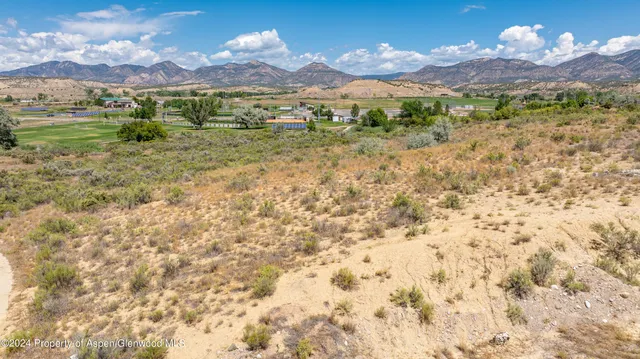 a view of a lush green hillside and houses with the view of mountains