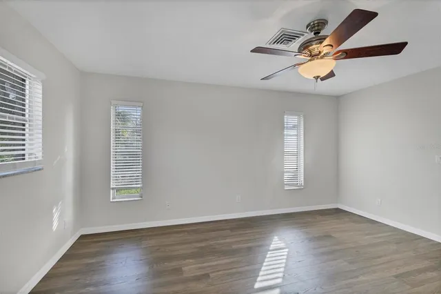 an empty room with wooden floor chandelier fan and windows