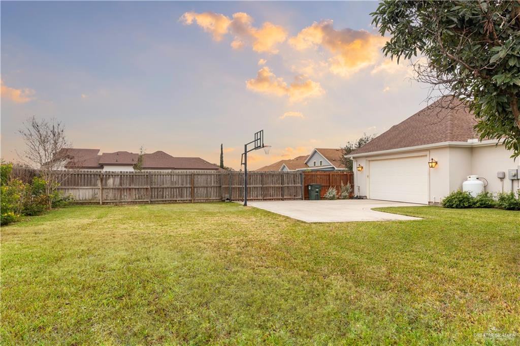 2701 Thompson Street Mission, TX 78573 - Photo 19 of 23 Yard at dusk featuring a fenced backyard, motorized gate, in-ground basketball hoop, and the two-car garage