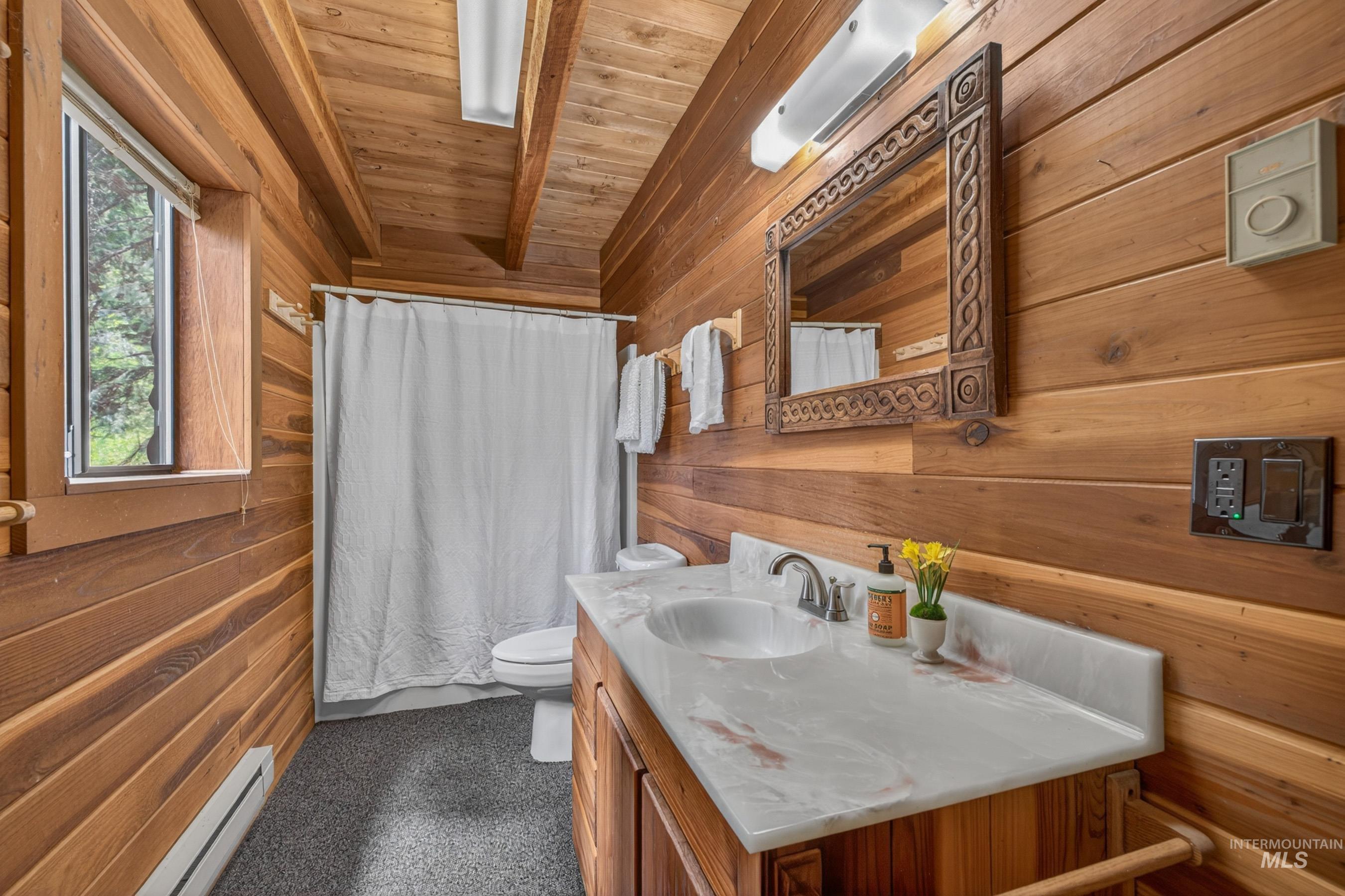 2339 West Mountain Road Donnelly, ID 83615 - Photo 14 of 37 Wood-paneled bathroom featuring a single vanity with an integrated sink and light-toned countertop, a decorative wood-framed mirror, and a window providing natural light