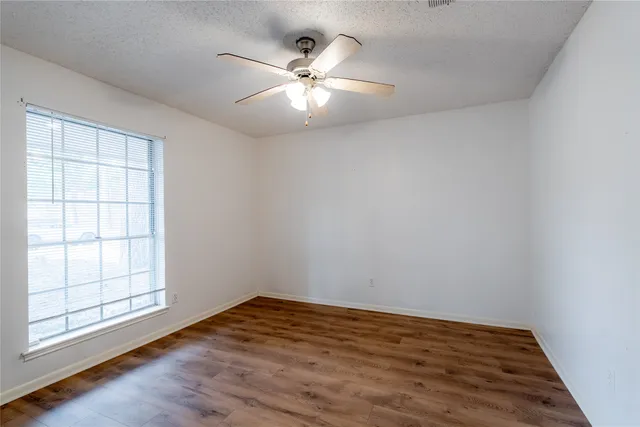 an empty room with wooden floor fan and windows