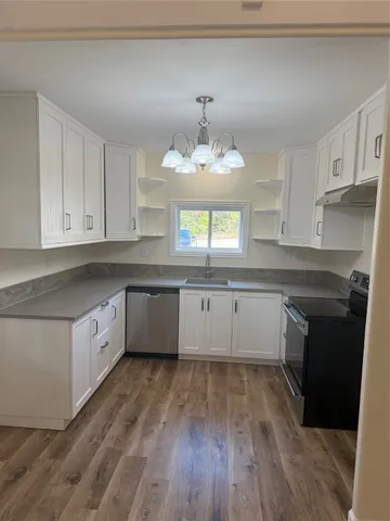 a large white kitchen with granite countertop a stove top oven a sink dishwasher and white cabinets with wooden floor