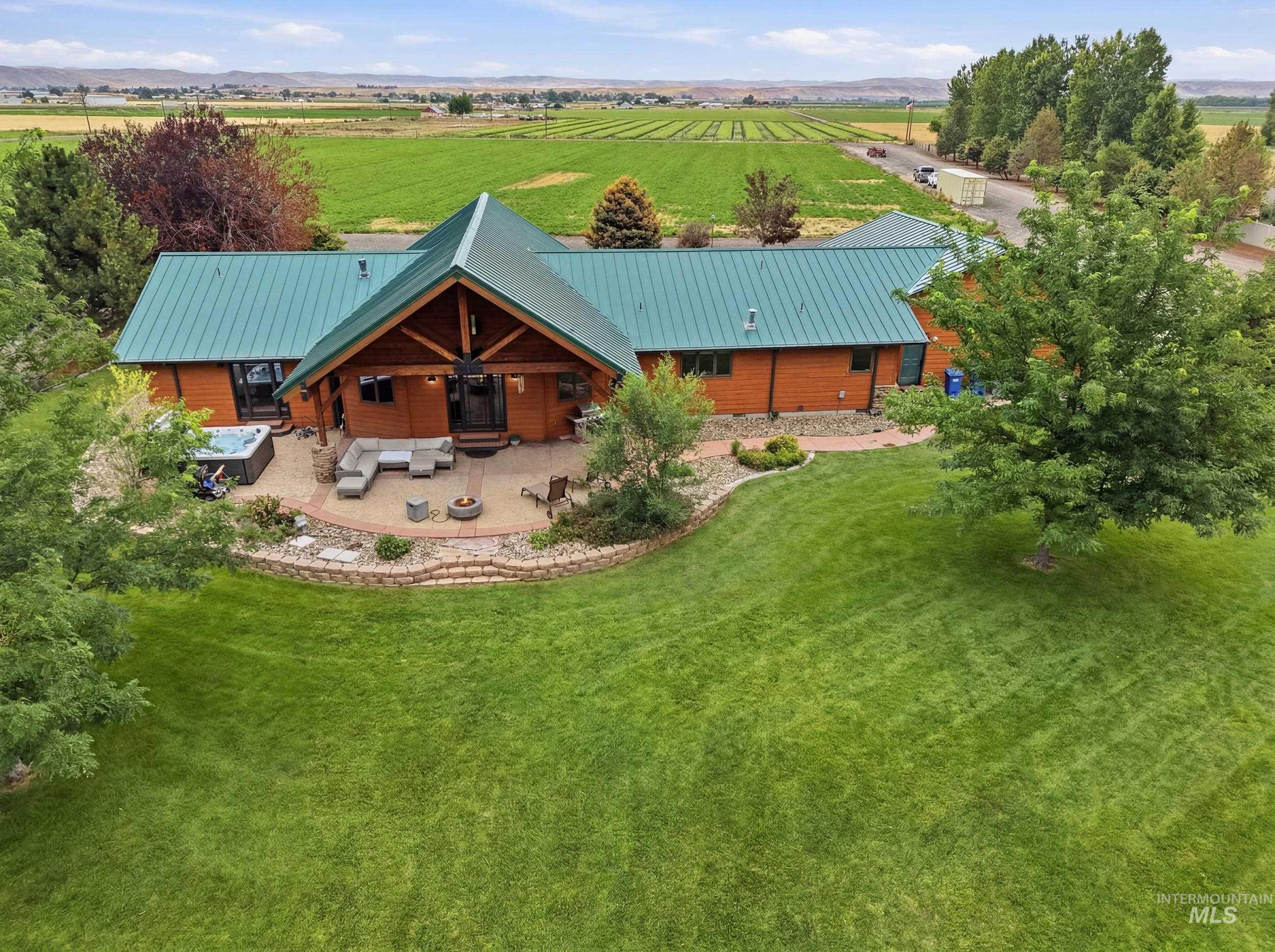339 Airport Road Weiser, ID 83672 - Photo 46 of 49 Wood-sided residence featuring a teal metal roof, a prominent covered patio with a vaulted ceiling, an integrated hot tub, and a surrounding expansive lawn