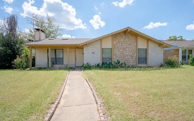 a view of a house with brick walls plants and large tree