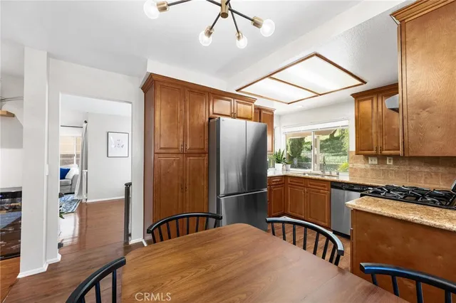 a kitchen with stainless steel appliances granite countertop a refrigerator a sink dishwasher a stove and a dining table with wooden floor