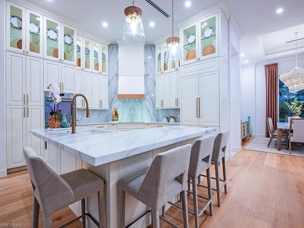 2363 Crayton Road Naples, FL 34103 - Photo 17 of 30 Gourmet kitchen featuring a substantial island with stone countertop, extensive custom cabinetry with glass-front uppers, a built-in oven, and wood-finish flooring