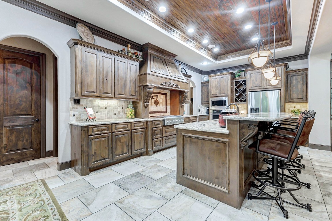 4315 Wickby Street Fulshear, TX 77441 - Photo 14 of 46 This spacious kitchen features elegant wood cabinetry, a coffered ceiling and modern stainless appliances. The large island offers seating and ample counter space, while pendant lighting adds a warm ambiance. Perfect for cooking and entertaining.