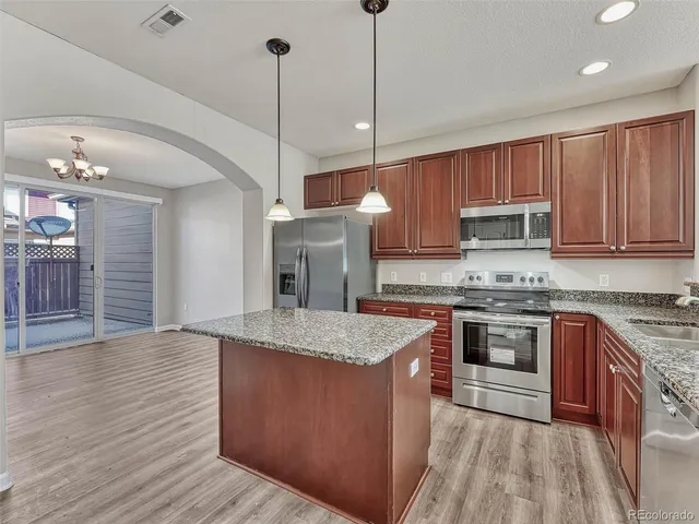 a kitchen with stainless steel appliances granite countertop wooden cabinets a sink a stove a kitchen island and chairs