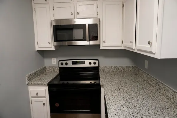 a kitchen with stainless steel appliances granite countertop white cabinets and a stove top oven