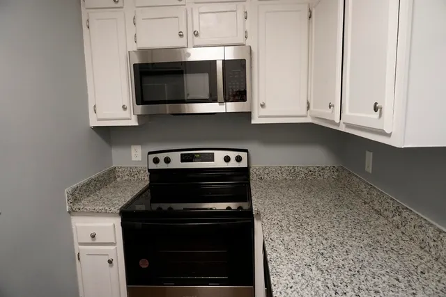 a kitchen with stainless steel appliances granite countertop white cabinets and a stove top oven
